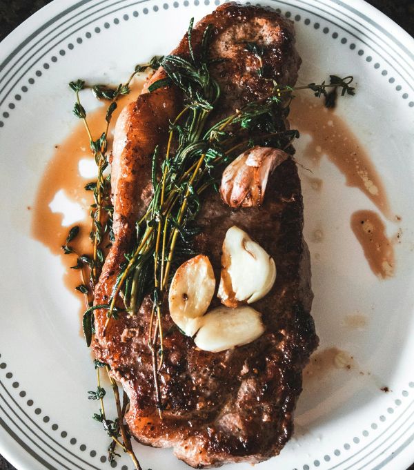 A juicy steak garnished with garlic and herbs on a white plate.