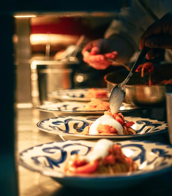 Chef plating pasta with sauce on decorative plates in a kitchen.