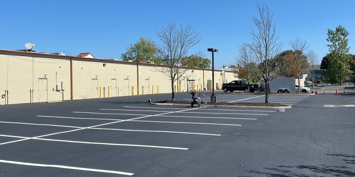 Empty parking lot with trees and buildings under clear sky.