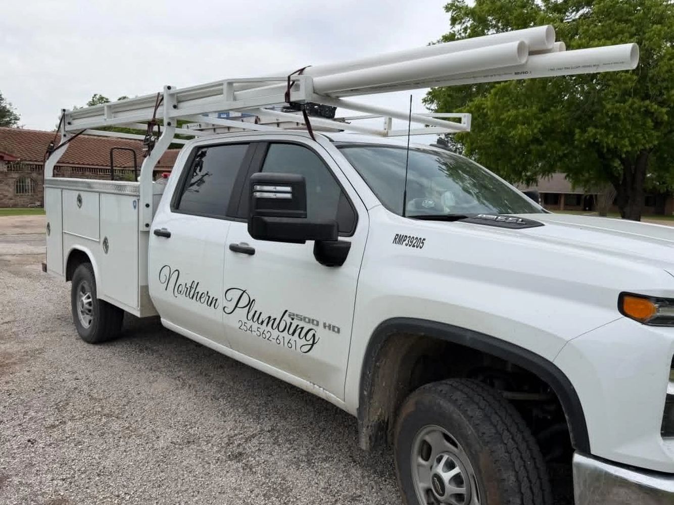 White plumbing service truck with pipes on top and company logo on door.