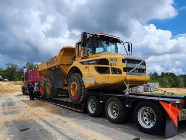 Heavy-duty yellow Volvo dump truck loaded on a flatbed trailer at a construction site.