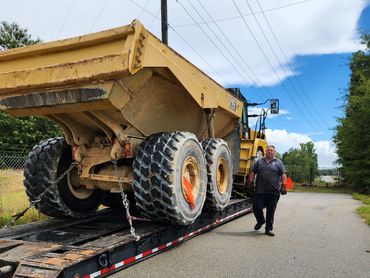 Man walking near a large yellow construction vehicle on a trailer.