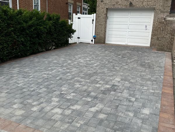 Newly paved gray stone driveway with brick border in front of a garage.