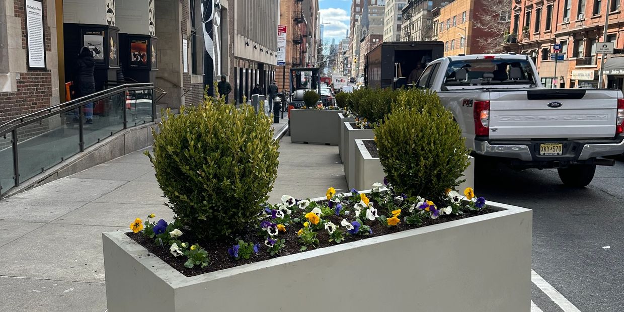 Urban street planters with flowers and shrubs under a partly cloudy sky.