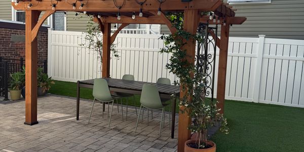 Wooden pergola with string lights over an outdoor dining table and green chairs.
