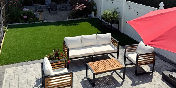 Modern backyard patio with cushioned seating and a red umbrella on stone tiles.