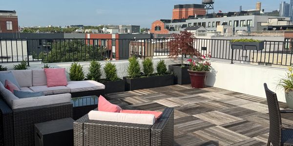 A rooftop patio with wicker furniture and cityscape views under a clear sky.