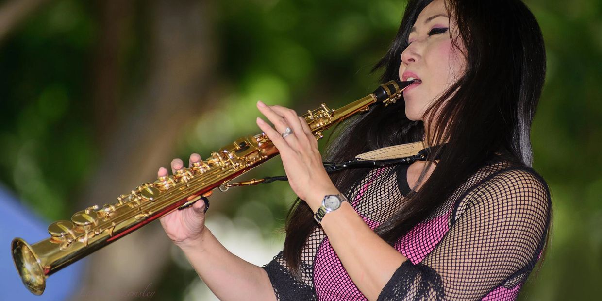 a young asian female playing soprano sax in fishnet outfit