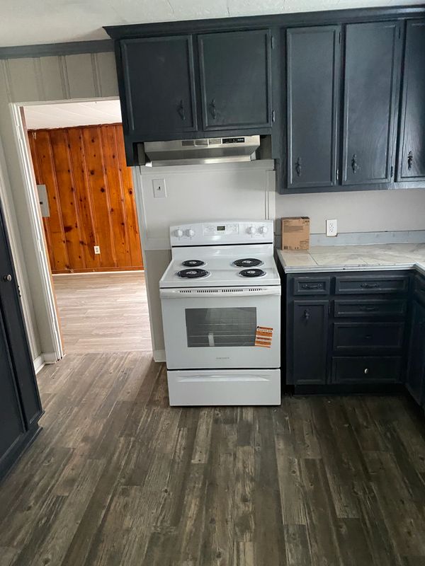 New stove installed in a kitchen remodel with new lap flooring and painted cabinetry.