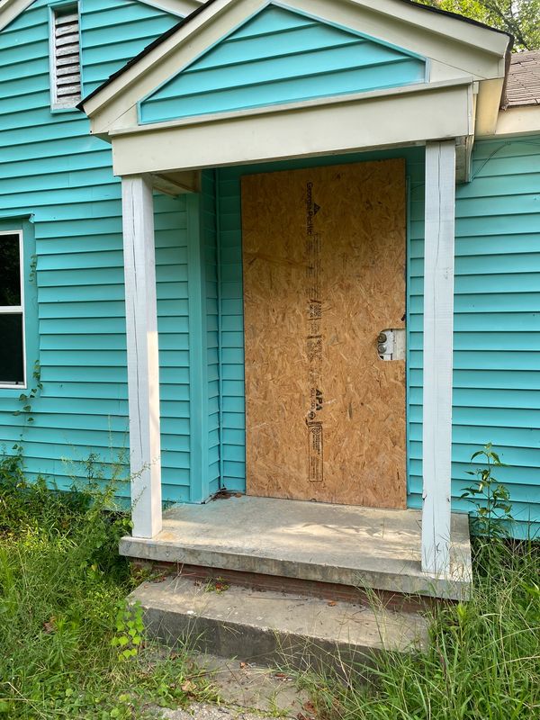 entryway of blue house with board over the front door of home in need of a full home remodel.