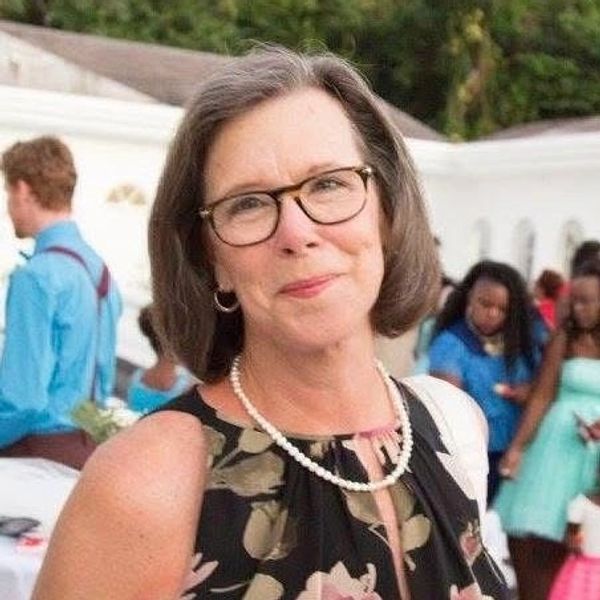 A woman with glasses and pearl necklace smiling at an outdoor event.