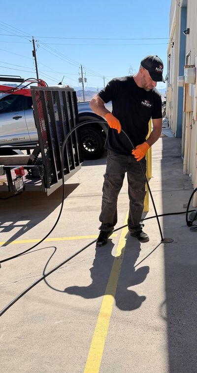 Man in black shirt and cap pressure washes a concrete surface outside.