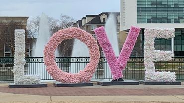 Large floral letters spelling LOVE in front of a fountain and buildings.