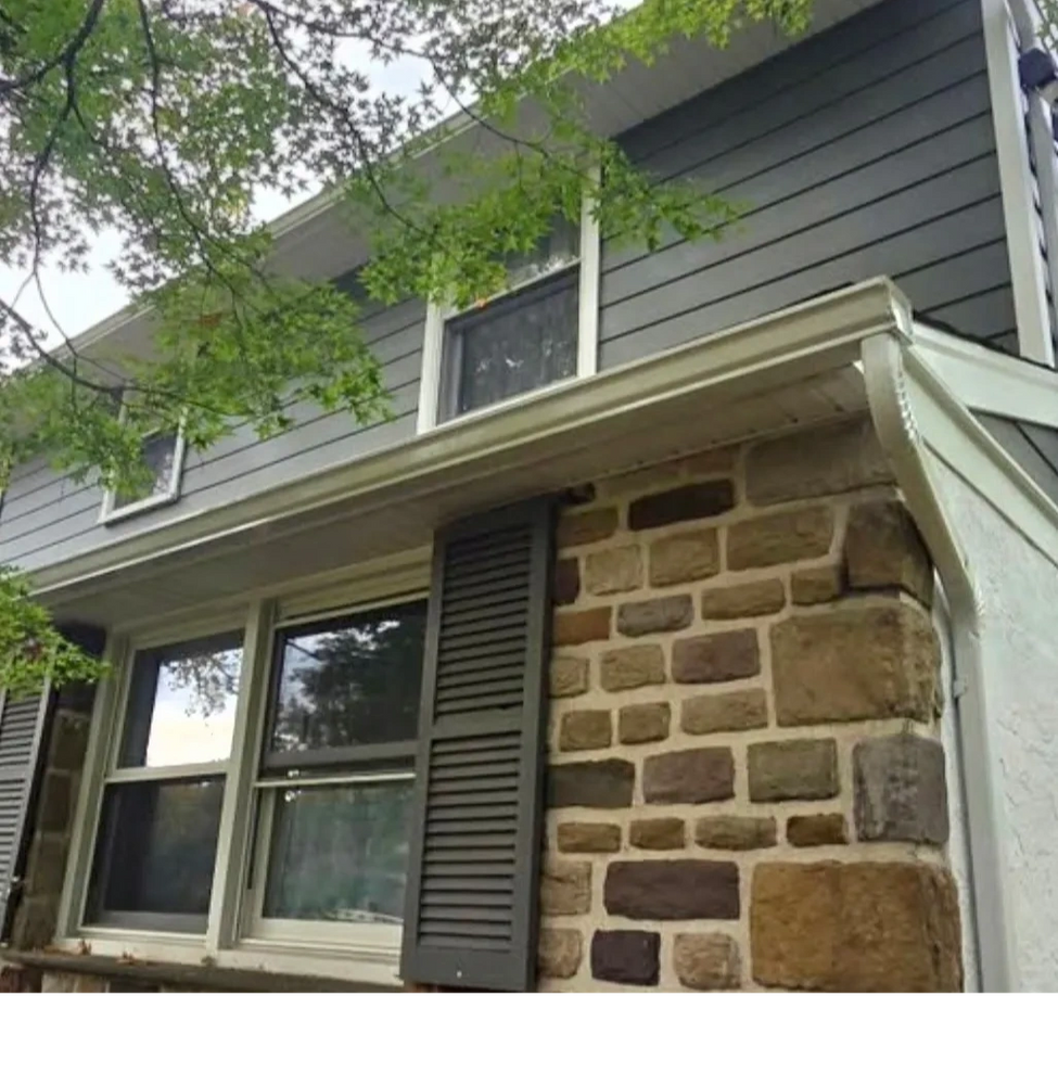 Two-story house with stone and siding exterior and leafy tree branches.