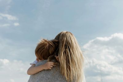 A woman with long hair embraces a child under a cloudy sky.