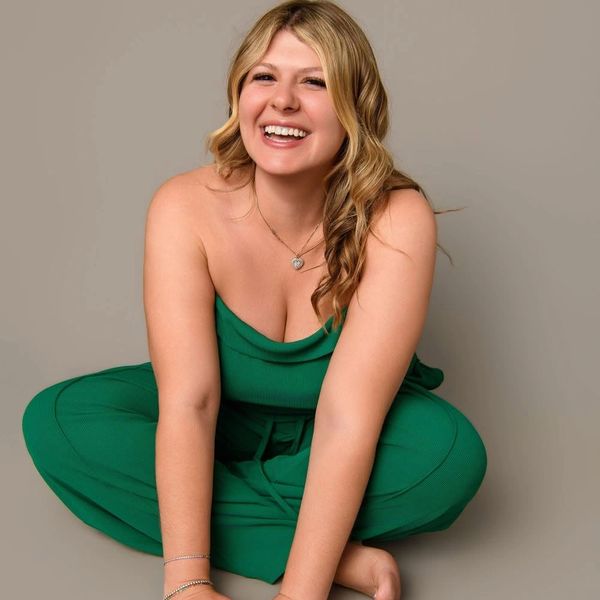 Smiling woman in a green outfit sitting cross-legged on the floor.