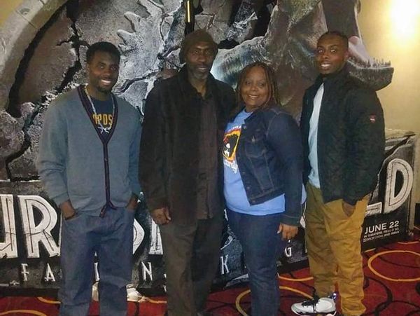 Four people posing in front of a Jurassic World poster.