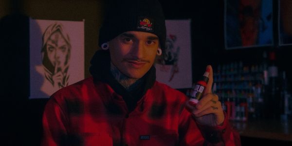 Man in red jacket holding a bottle of liquid ink, in a dimly lit room.