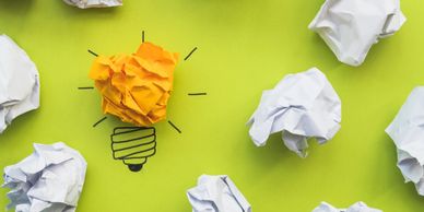 A picture of several crumpled up pieces of paper, with one that is gold and illustrated as a light b