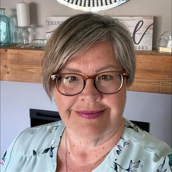 A smiling mature woman with glasses and short gray hair in a floral top.