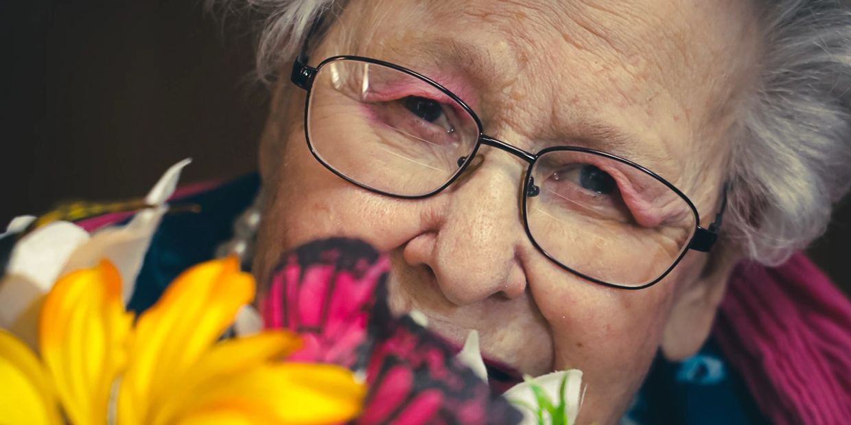 An elderly woman playfully looks up through a bouquet of silk flowers.