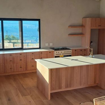 Modern kitchen with wooden cabinets, white countertops, and a large window showing a scenic view.