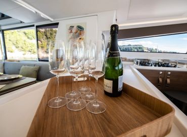 Champagne bottle and glasses on a wooden tray inside a modern yacht.
