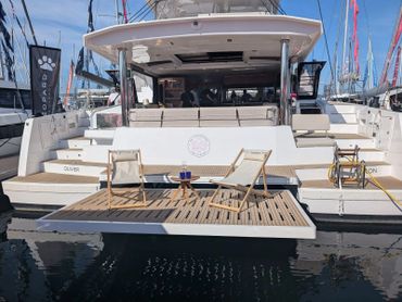Modern catamaran with deck chairs and a small table, docked at a marina.