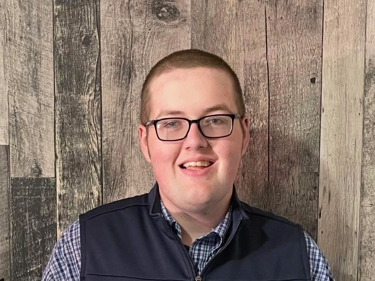 A smiling man with glasses in front of a wooden backdrop.