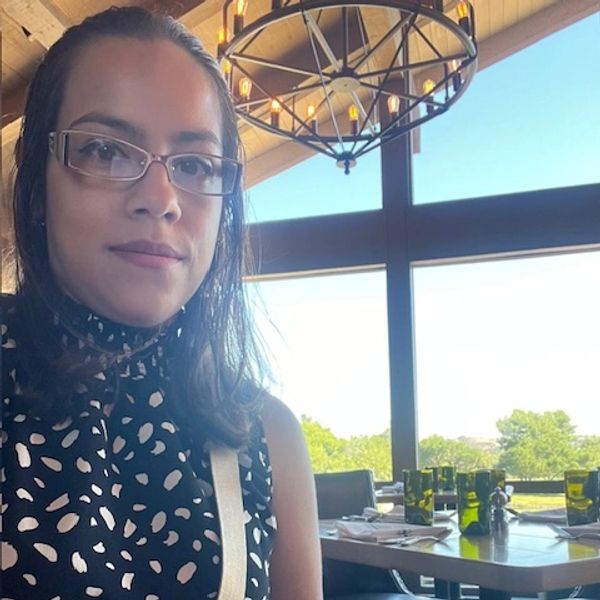 Woman wearing glasses sitting in a restaurant with large windows and natural light.