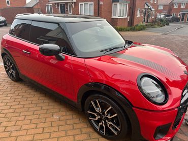 Red Mini Cooper with black roof and racing stripes parked on driveway.
