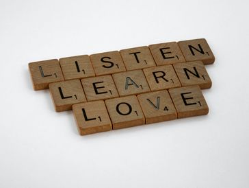 Scrabble tiles arranged to read “Listen,” “Learn,” and “Love,” symbolizing compassion and empathy.