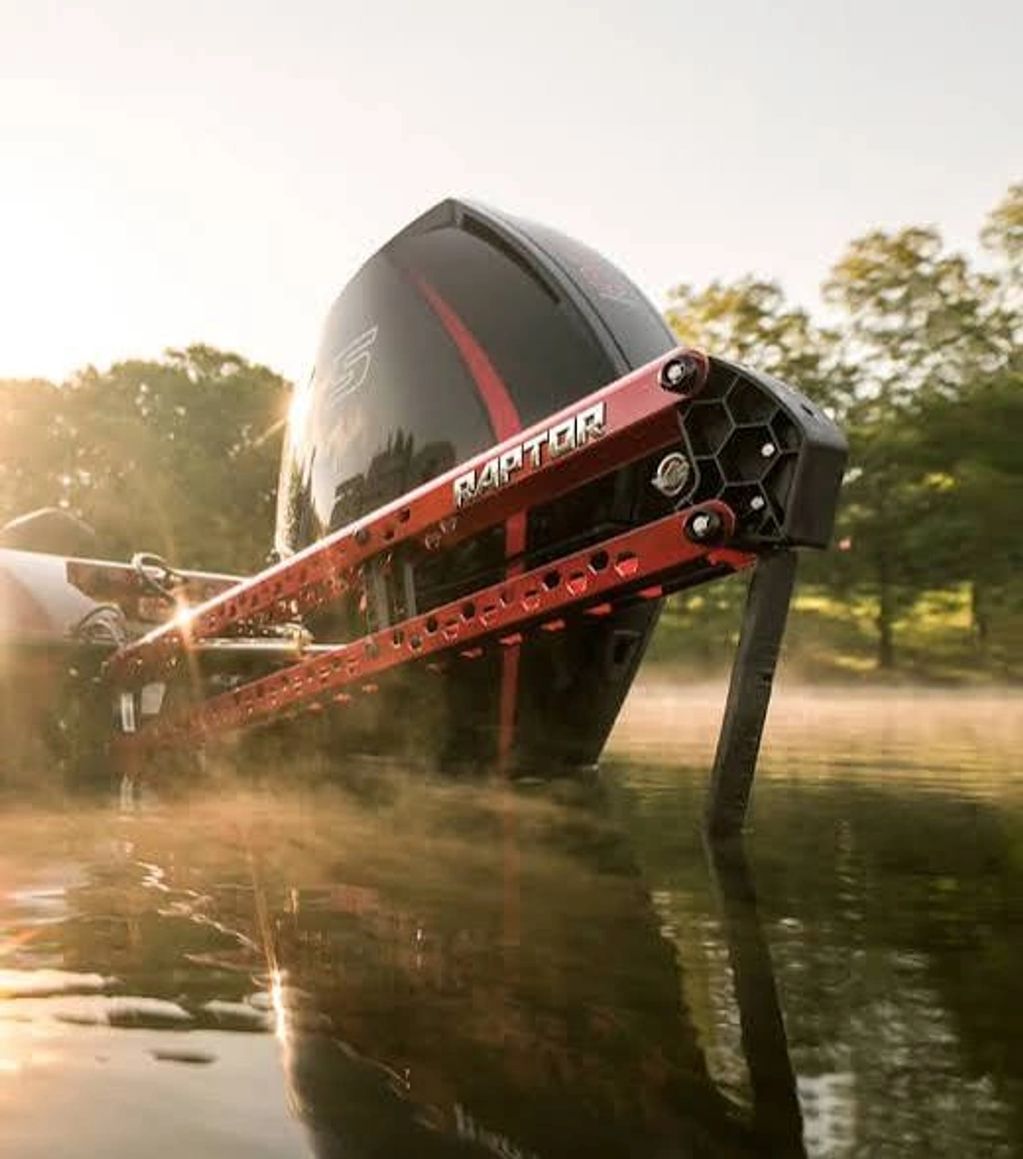 Close-up of a boat motor with a Raptor attachment in calm water at sunrise.