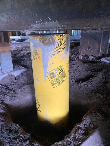 Yellow concrete form tube in a hole under a structure.