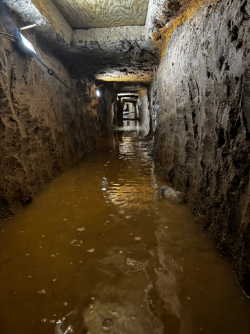 A flooded underground tunnel with rough walls and dim lights.