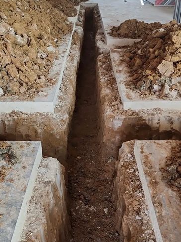 Deep trench dug in soil at construction site.