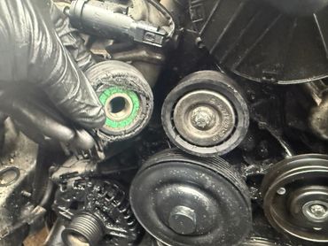 Close-up of car engine pulleys and belts showing wear and grime.