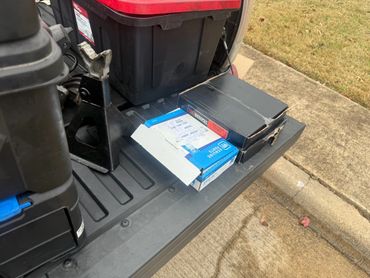 Boxes of automotive parts and a jack stand on a vehicle's tailgate.