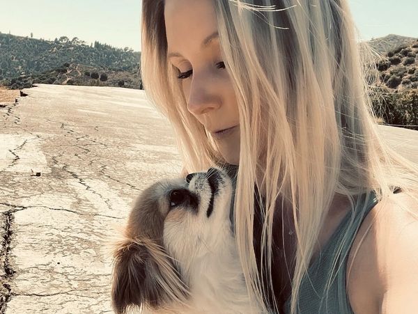 A woman lovingly holds and looks at her small dog outdoors on a sunny day.