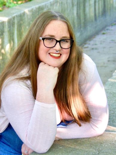 Woman with glasses smiling outdoors.