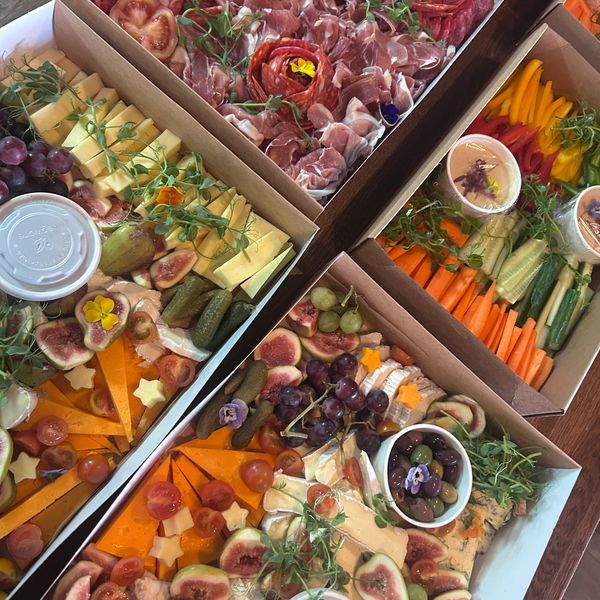 Gourmet charcuterie and vegetable boxes with cheeses, meats, fruits, and dips.