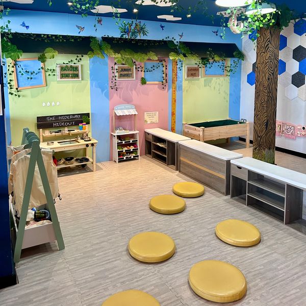 Colorful children's playroom with themed activity stations and yellow floor cushions.