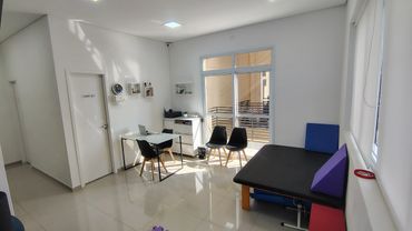 Imagem ampla da sala de terapia, com tablado a direita e mesa a esquerda. Varanda ao fundo.