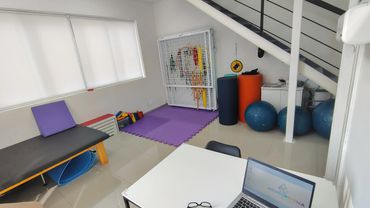 Imagem ampla da sala de terapia, com tablado a esquerda, mesa a direita e gaiola de habilidades.