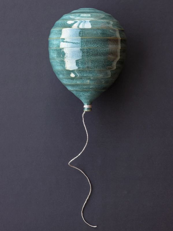 A ceramic balloon-shaped object with a string attached, displayed on a dark background.