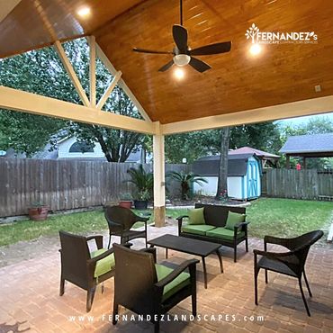 Patio cover with a wood ceiling and fan over a brick paver patio