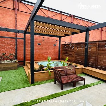Small backyard with a black slat pergola, artificial turf and a wood bench