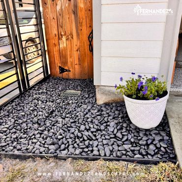 Black river pebbles and a flower pot beside a garden gate