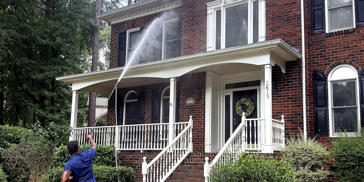Man power washing a brick house's porch.