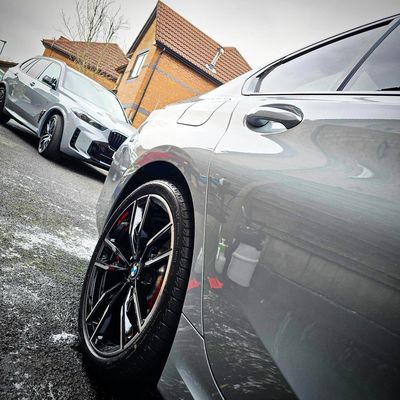 Two sleek silver BMW cars parked on a driveway near houses.